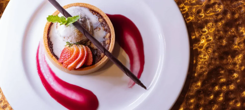 A delicious dessert tart featuring sliced strawberry, vanilla ice cream, and chocolate garnish is offered at our Santa.