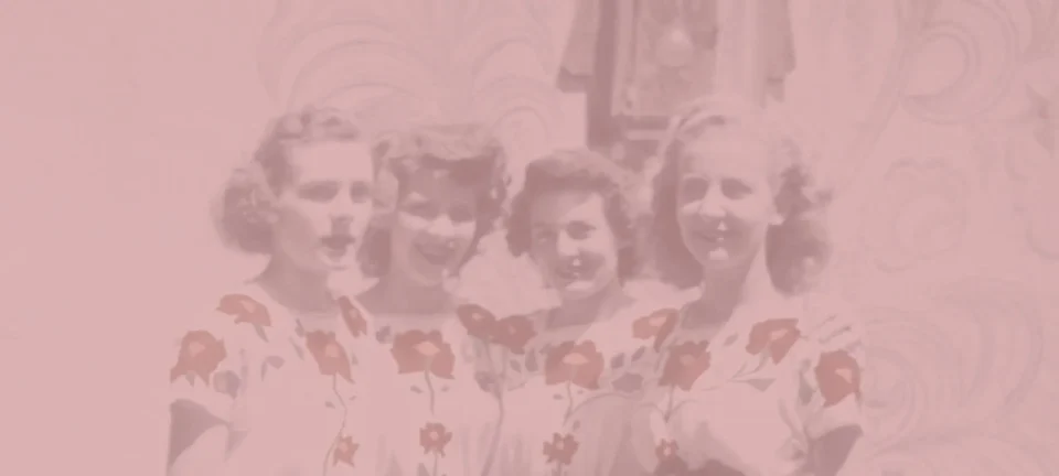 Four smiling women in floral print dresses are visible in this heavily pink-faded archival photograph.