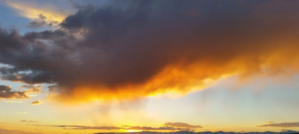 A massive, dark storm cloud dominates the sky, backlit by the intense orange and gold light of the setting sun.