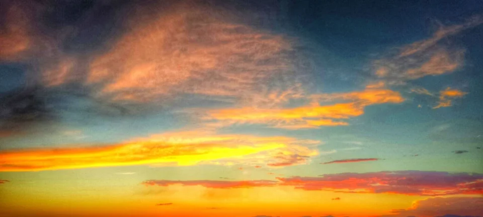 The vibrant sky is painted with fiery orange, yellow, and teal clouds during a breathtaking sunset.