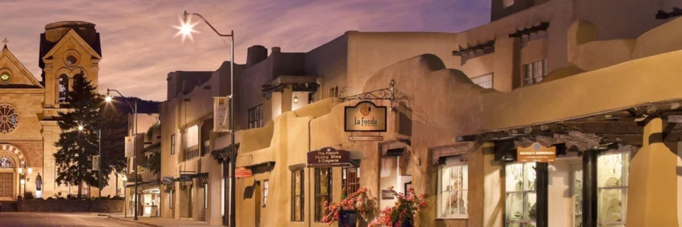 The warm, adobe-style exterior of La Fonda on the Plaza is brightly lit along the street near the historic cathedral.