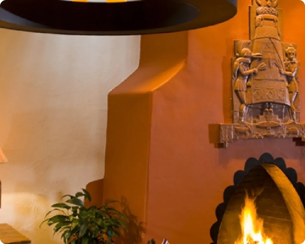 An ornamental kiva fireplace burns brightly in the corner of a luxurious hotel suite.