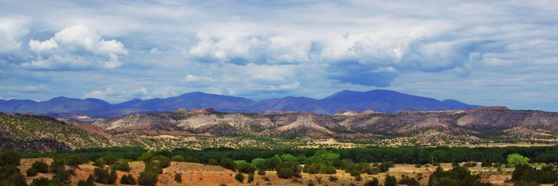 A panoramic view shows arid foothills and a green valley leading toward hazy blue mountain peaks.