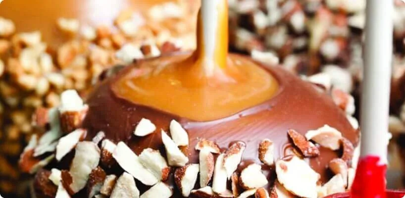 A decadent candy apple is thickly coated in melted chocolate, rich caramel sauce, and chopped nuts.