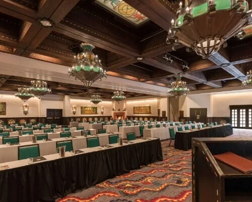 A grand banquet hall is arranged in a classroom setup for an event, featuring ornate green chandeliers and a dark wood.