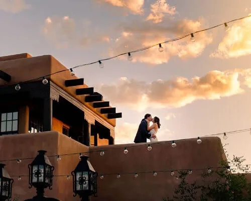 A newly married couple kisses on a beautiful adobe rooftop, showcasing the perfect wedding venue setting.