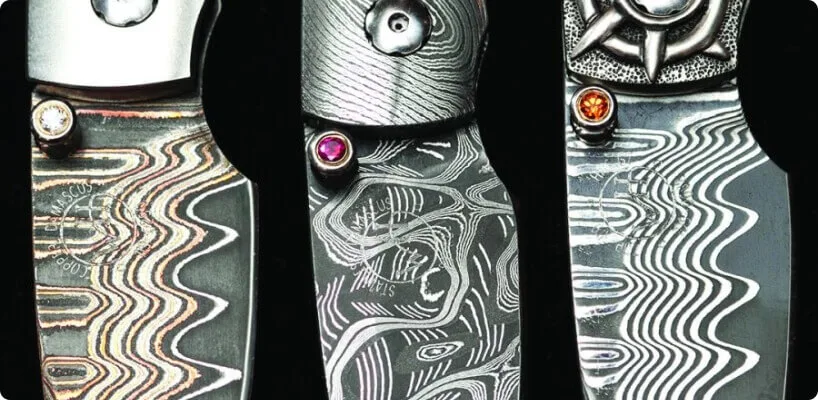 Three highly detailed custom metal handles showcase swirling Damascus steel patterns and small polished gemstones.