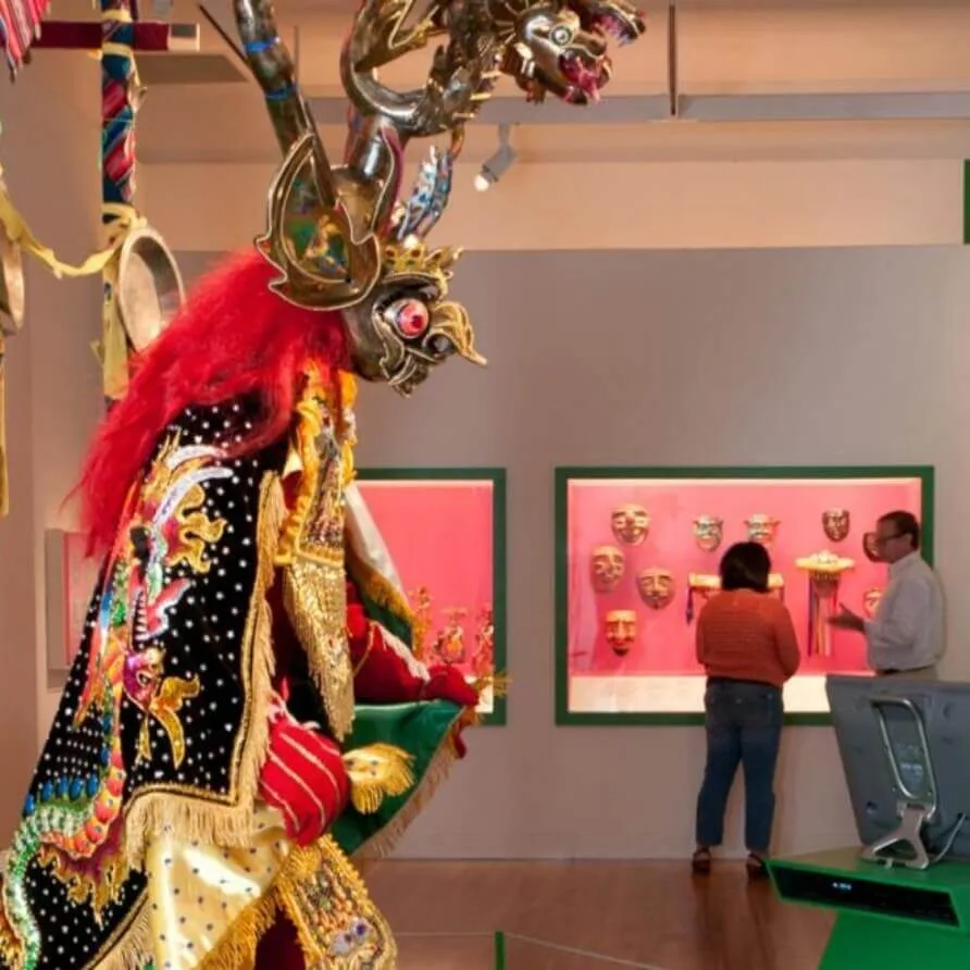 An elaborate gold and red ceremonial mask and costume are displayed inside a museum gallery.
