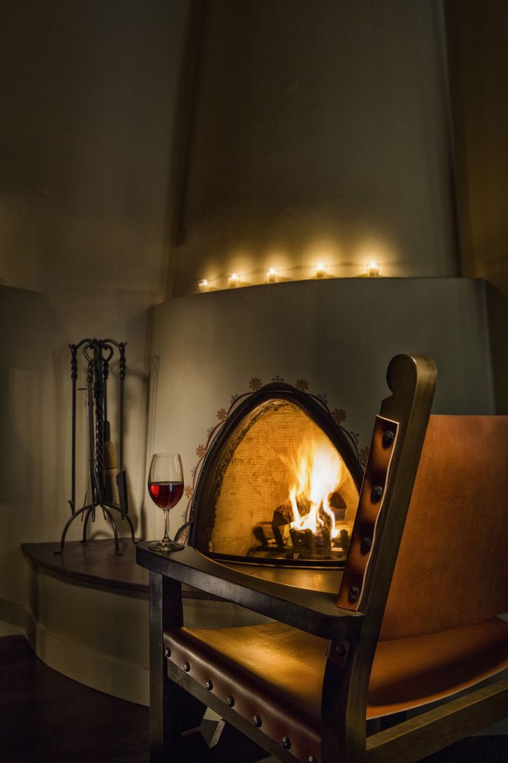 A cozy kiva fireplace burns brightly next to a leather chair and a glass of red wine in a hotel suite.
