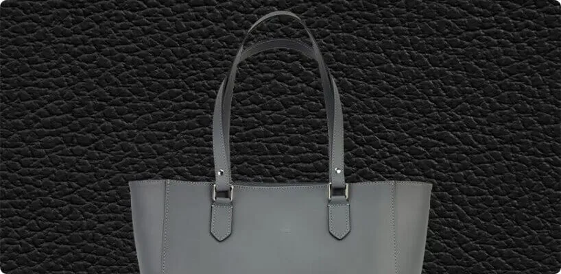A sophisticated gray leather tote bag featuring two handles is displayed against a deeply textured black leather.