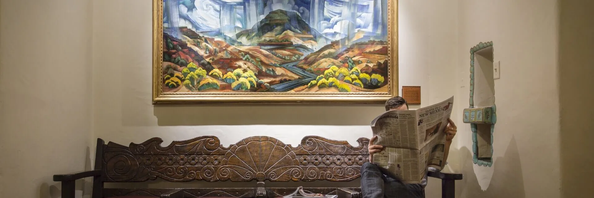A guest relaxes on a carved wooden bench beneath a colorful landscape painting in the historic lobby.