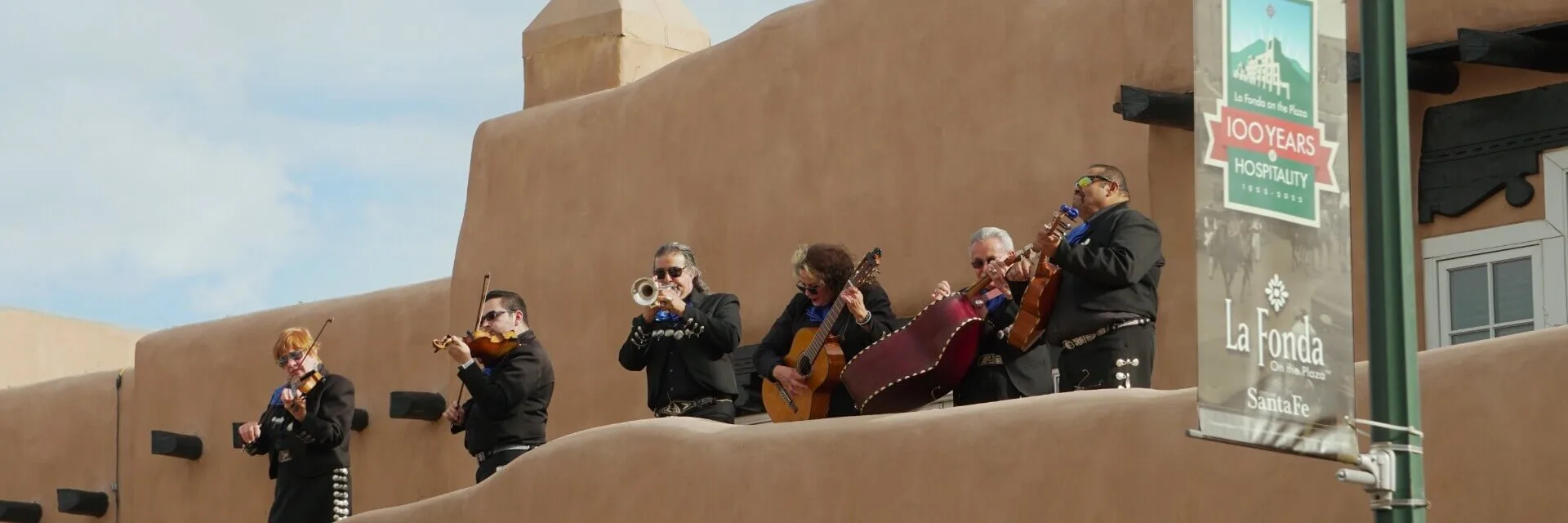 A five-piece band plays festive live music with violins, trumpets, and guitars from atop the adobe structure.