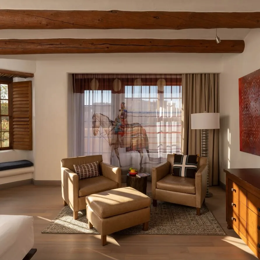 This spacious santa fe hotel room features a comfortable leather seating area below rustic wooden vigas.