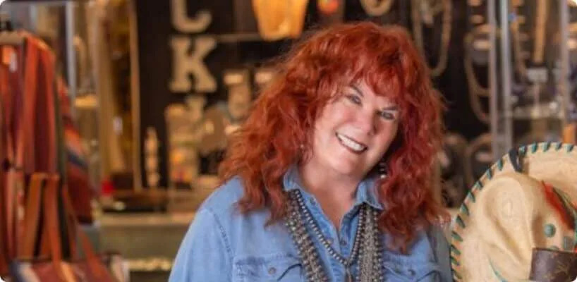 The happy woman with bright red hair wears multiple strands of silver beads and a denim shirt.