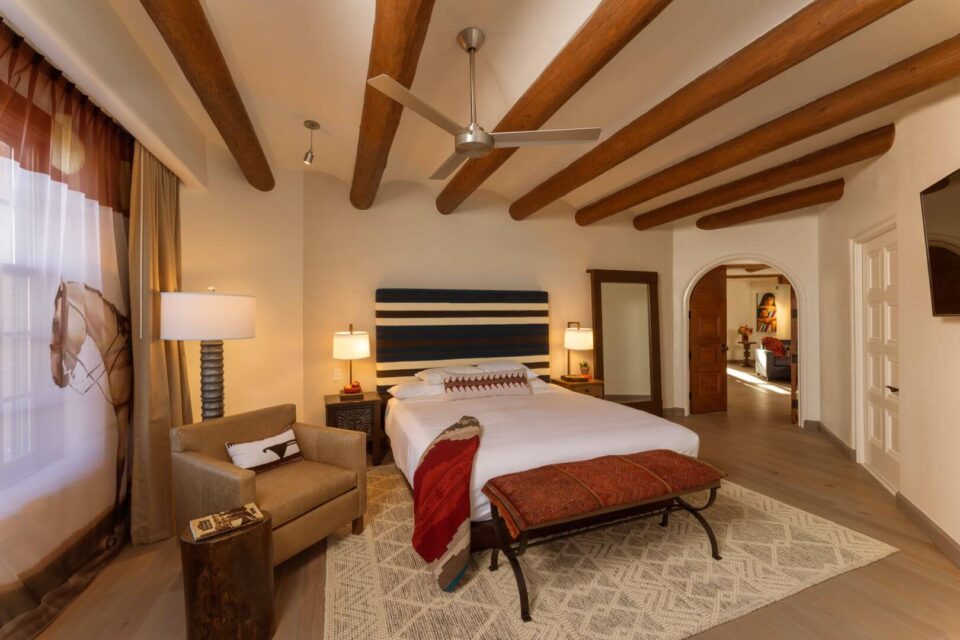 This spacious hotel suite bedroom has a king bed, beautiful Southwestern decor, and rustic wooden ceiling vigas.
