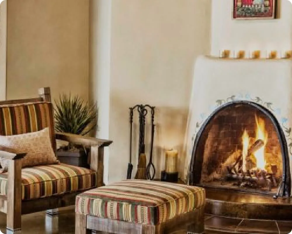 A brightly burning kiva fireplace warms a small seating area featuring a striped rustic armchair and ottoman.