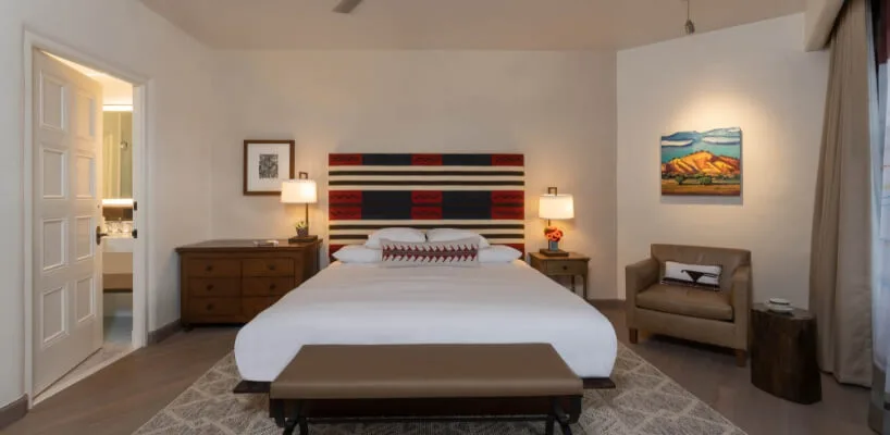 The spacious santa fe hotel room is decorated in New Mexican style, including a dresser, armchair, and custom headboard.