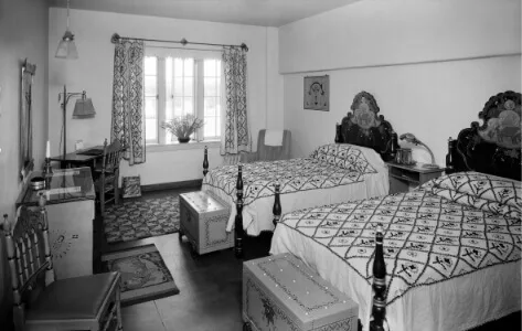 A vintage guest room features two twin beds with carved wooden headboards and hand-painted chests.
