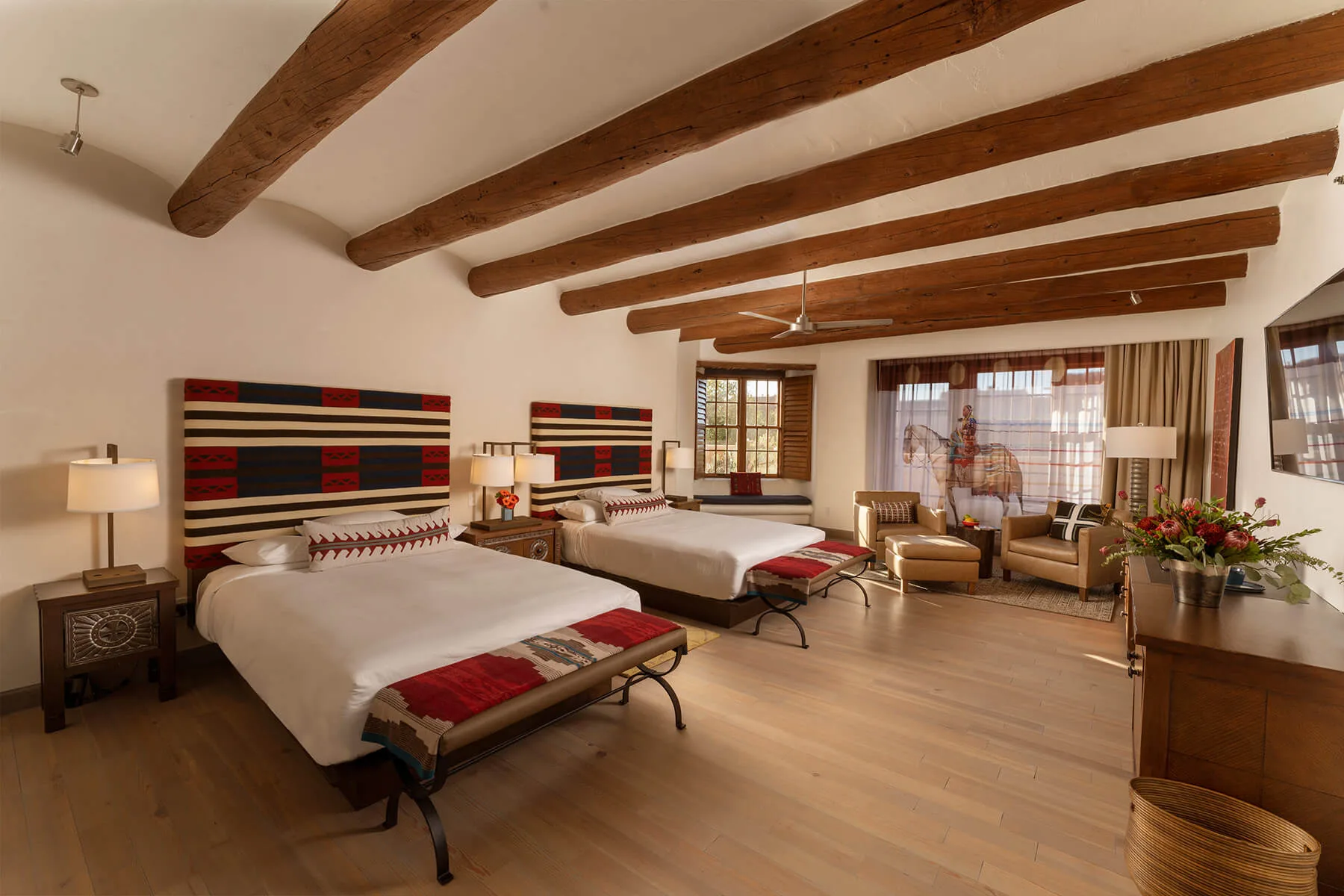 A beautifully appointed hotel room displaying two beds, wooden vigas, and rich Southwestern textiles.