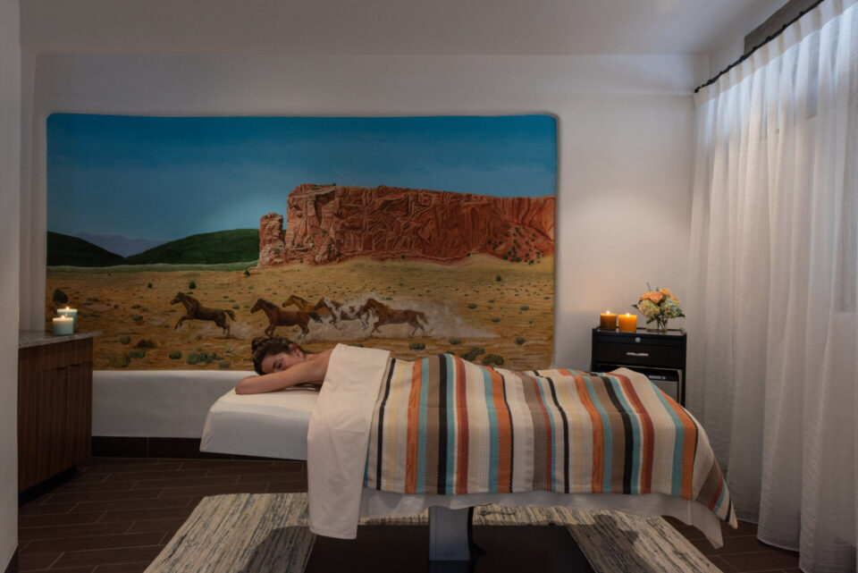 A guest rests face down on a spa treatment table covered by a striped blanket and illuminated by candlelight.