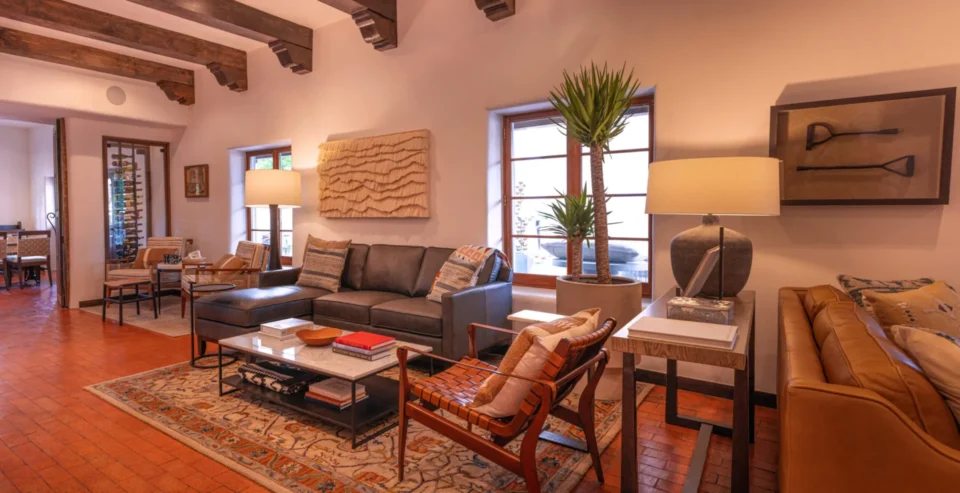 This elegant hotel suite living room features a leather sofa, marble coffee table, and exposed vigas.