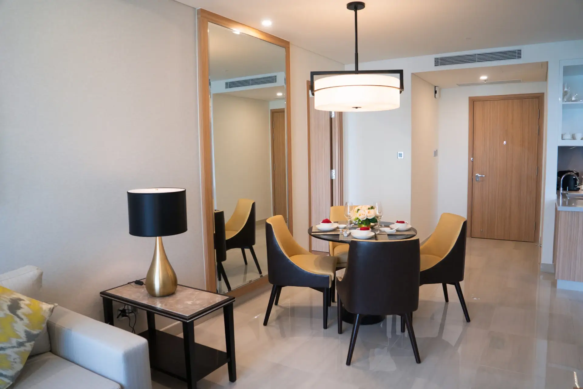 This bright, modern hotel suite features a round dining area with four chairs and a contemporary gold and black lamp.