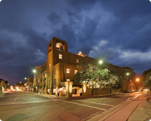 This Pueblo Revival style exterior of the boutique hotel is lit brightly at dusk on a downtown corner.