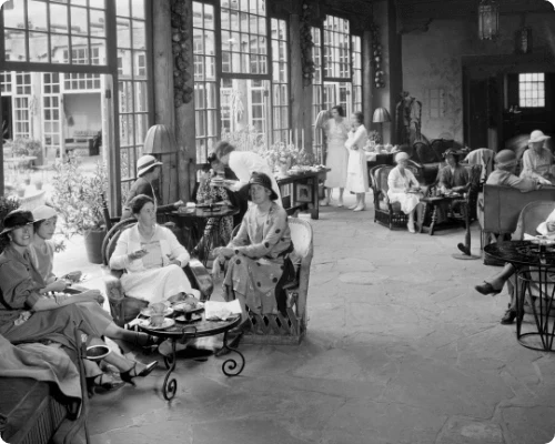 This historic image captures hotel guests enjoying afternoon tea inside the beautiful sunlit lounge.