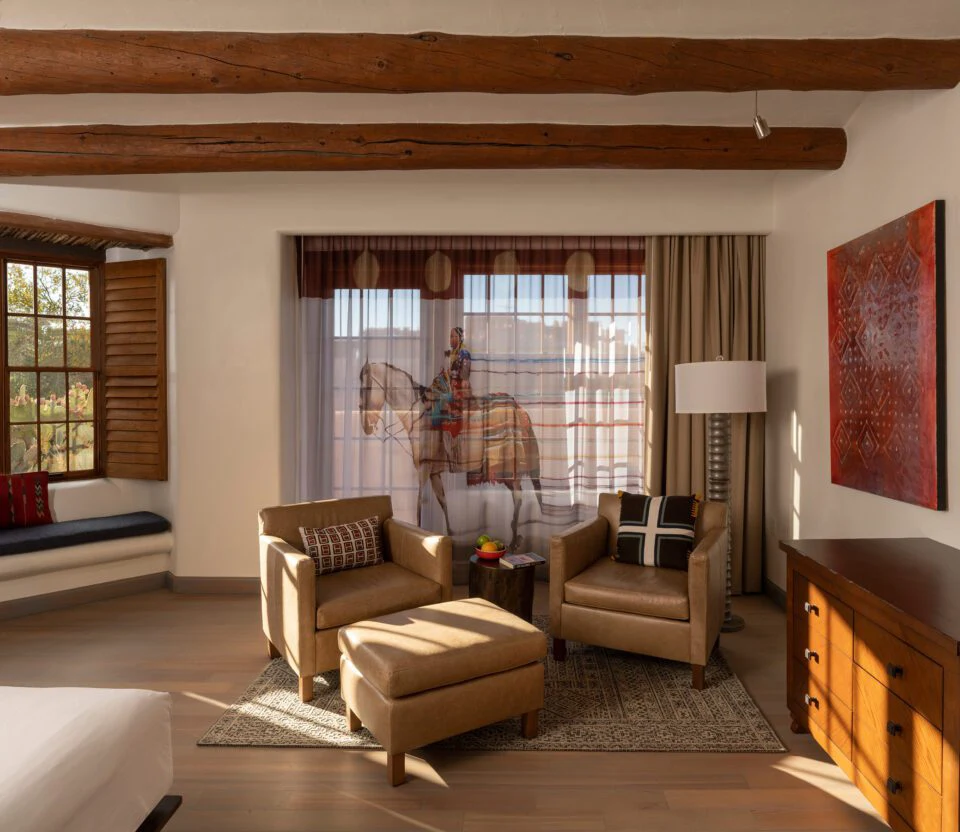 The cozy seating area of a luxury hotel suite includes leather armchairs, wooden vigas, and natural light.