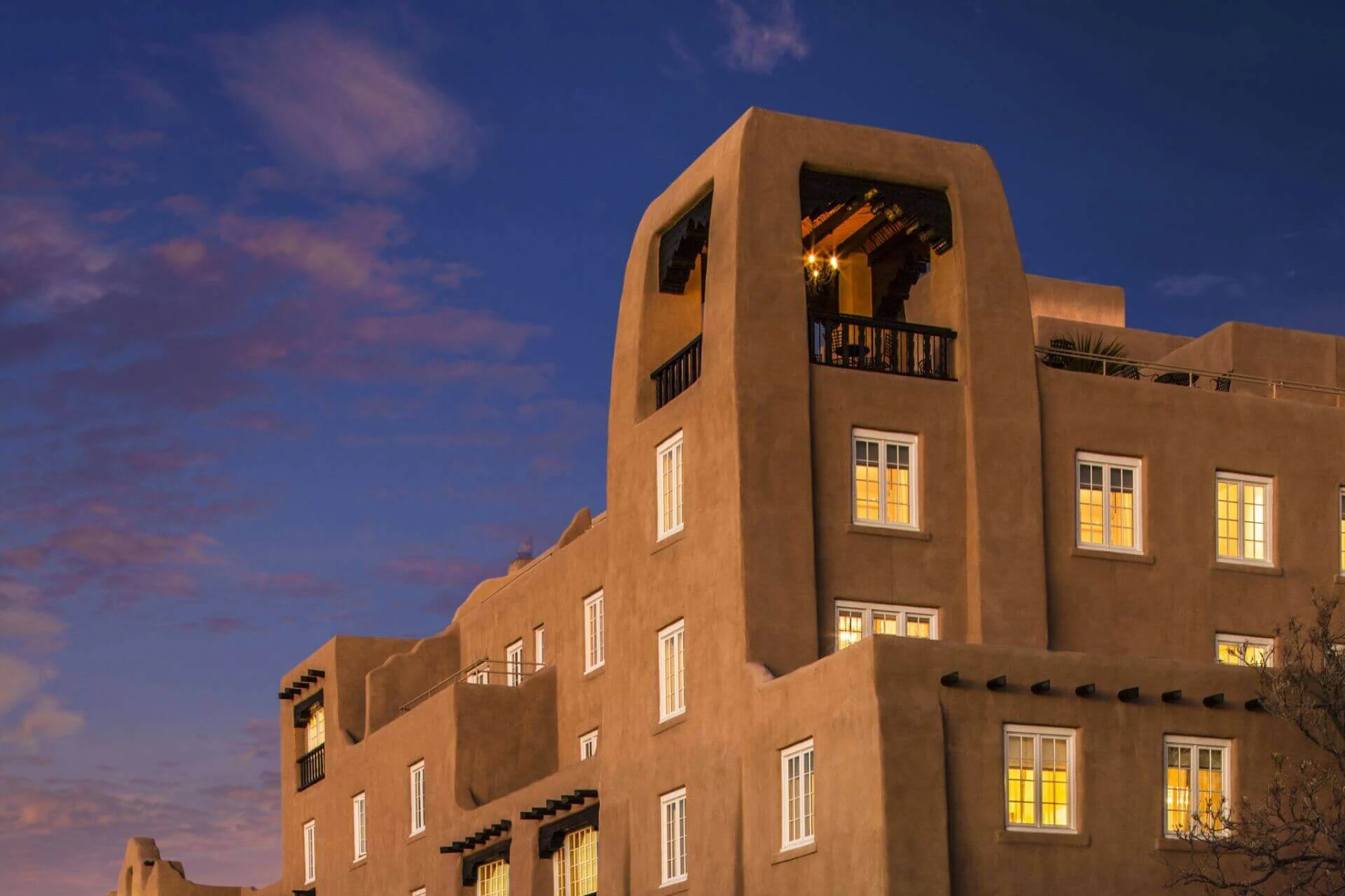 The terracotta adobe exterior of the historic hotel is illuminated against the deep purple twilight sky.