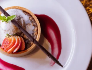 A gourmet plated dessert features a fruit tart topped with ice cream, sliced strawberries, and a chocolate garnish.