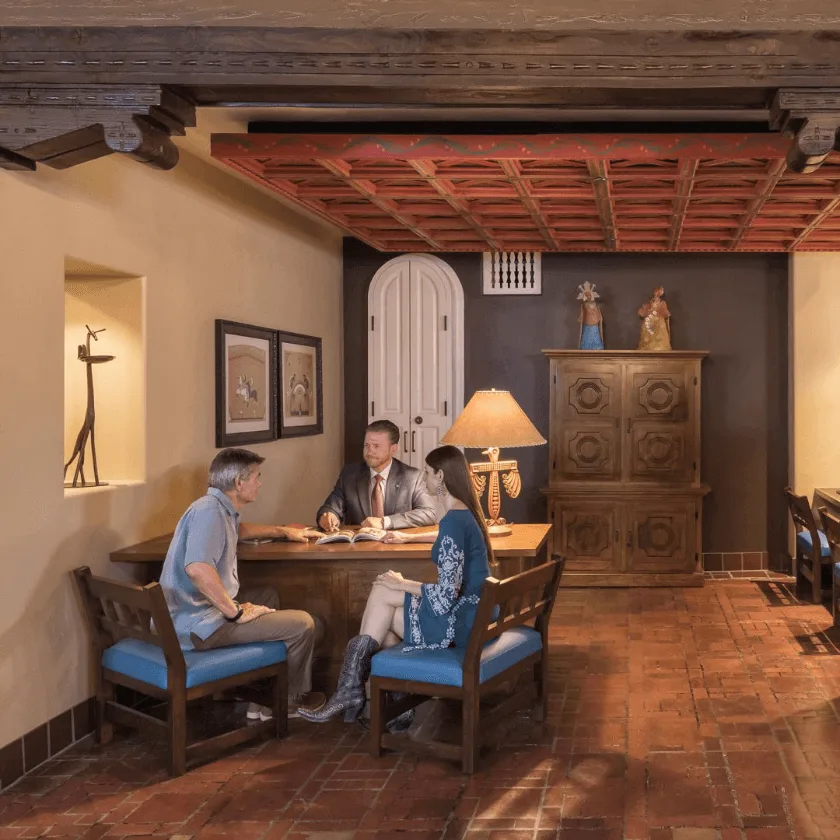 A hotel manager meets with a couple at a carved wooden desk in a room designed for planning event spaces.
