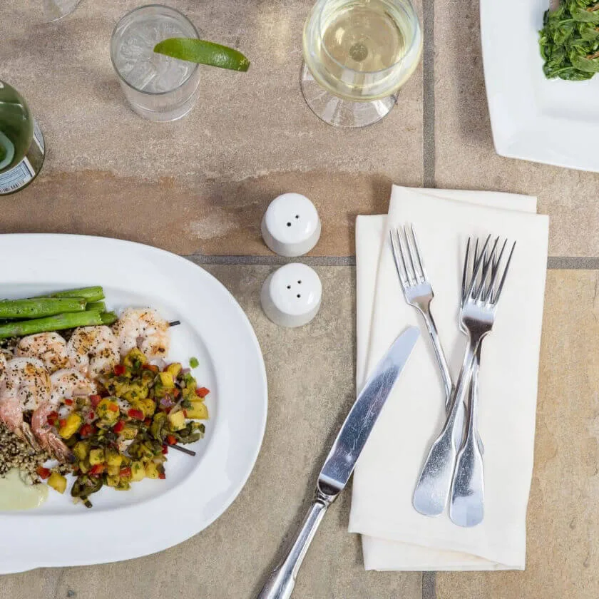 An overhead shot shows a fresh grilled shrimp and quinoa dish alongside wine and a cocktail at the restaurant.