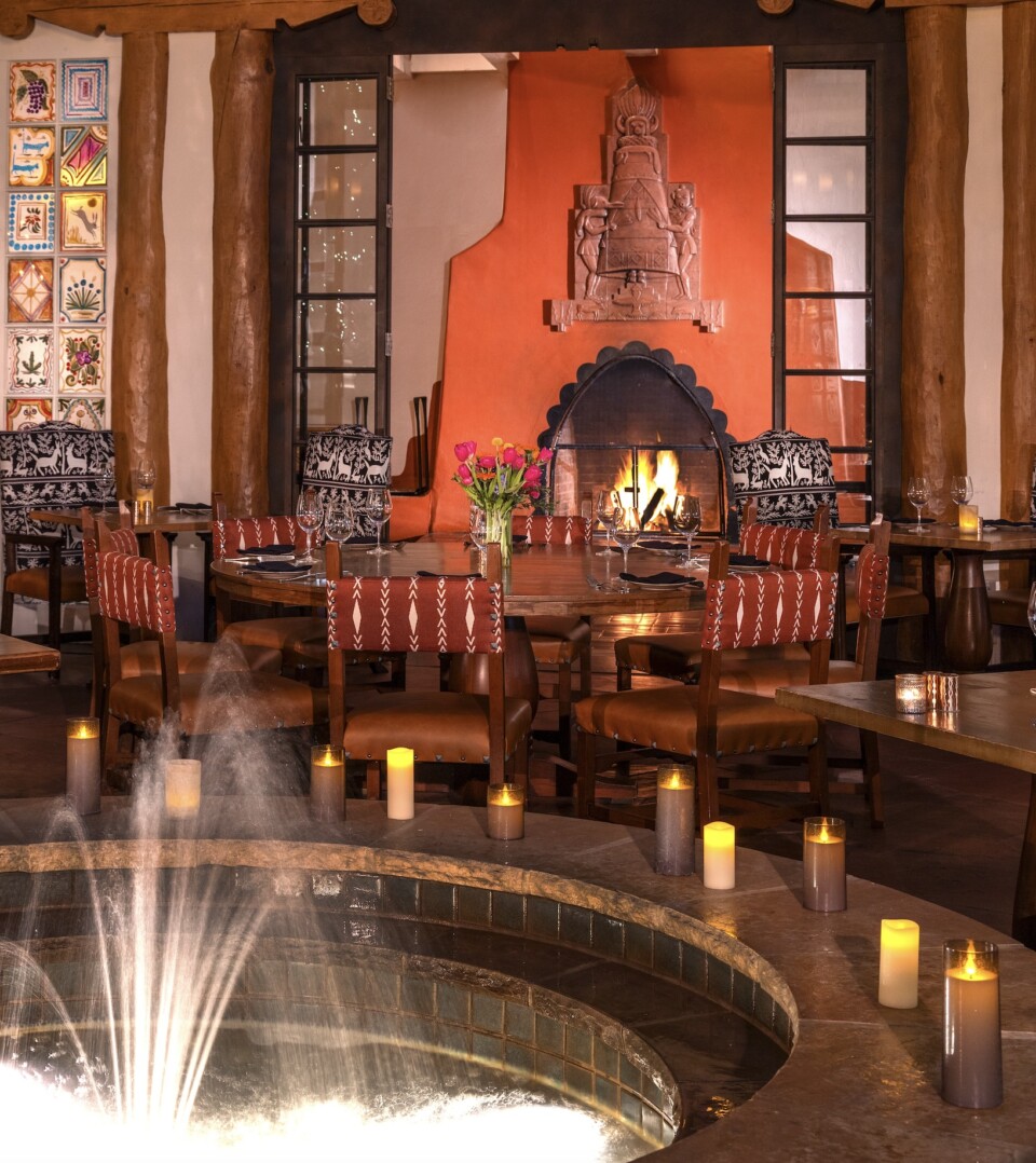 Two guests enjoying lunch and wine together inside La Plazuela restaurant, seated by a window overlooking the historic Santa Fe Plaza.