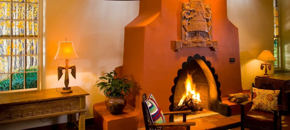The spacious hotel suite living area features a traditional adobe fireplace, artistic wooden furniture, and custom.