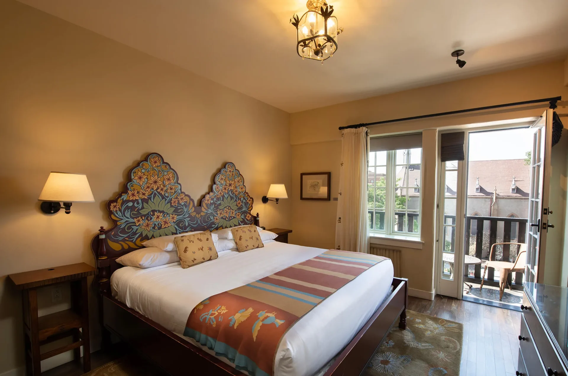 This beautifully appointed hotel room features an artistic, hand-painted headboard and a doorway leading out to a.