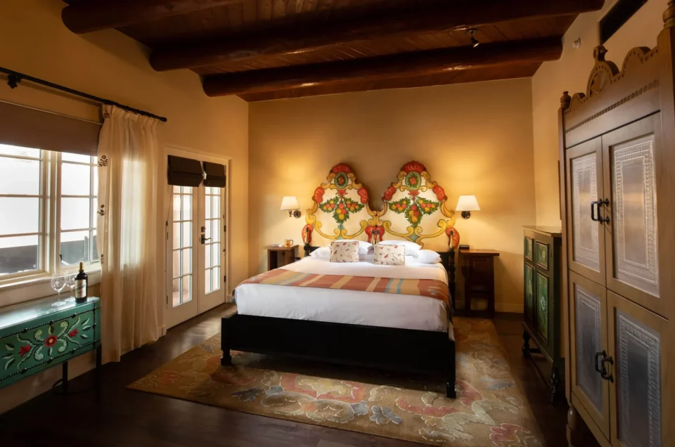 This gorgeous Santa Fe hotel room features traditional wooden vigas, a king bed, and a vibrant painted headboard.