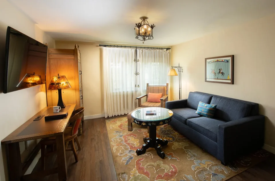 An elegant living space inside the hotel suite, showcasing a dark blue sofa, glass table, and patterned area rug.