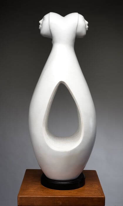 The elegant white sculpture features two profile heads atop an abstract body with a stylized teardrop cutout.