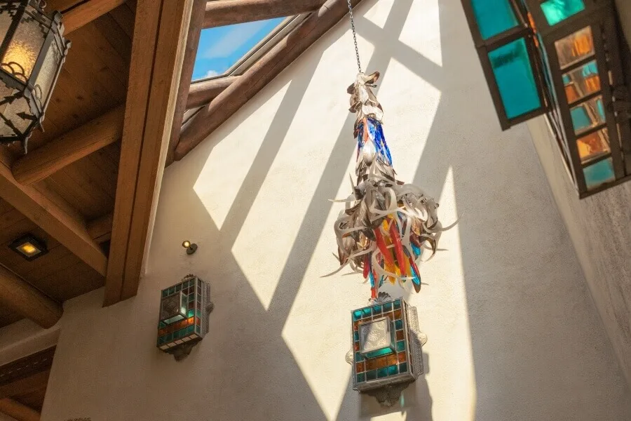 Sunlight highlights a creative antler light fixture and colorful stained glass sconces against a stucco wall.