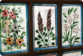 A close-up shows three blue-framed window panes featuring detailed hand-painted floral art.