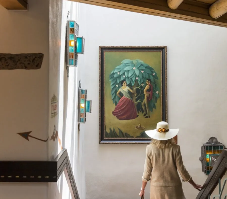 A woman in a tan suit ascends a stairwell featuring a large framed painting and custom decorative wall sconces.
