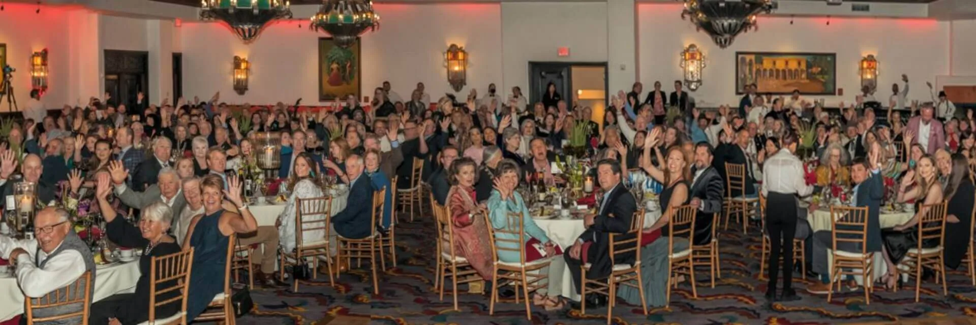 Guests are cheering while seated at round tables during a large gathering inside the ornate santa fe banquet hall.