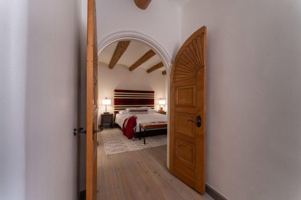 A partially open, carved wooden door reveals a luxurious Southwestern-style hotel room.