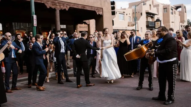 A joyful bride and groom dance with guests while a mariachi band performs celebratory live music.