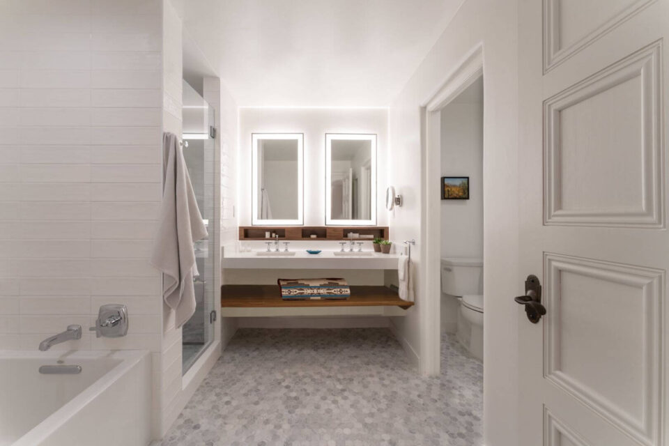 This bright, modern hotel room bathroom features a double vanity, white subway tile, and a walk-in shower.