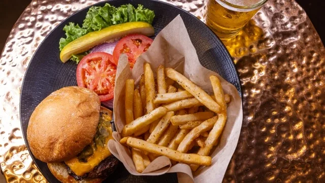 A delicious cheeseburger with seasoned fries and a cold beer is ready to be served in one of the hotel restaurants.