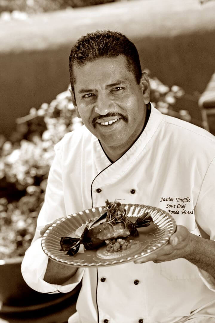 Sous Chef Javier Trujillo smiles while holding a meticulously plated entree dish ready to be served.