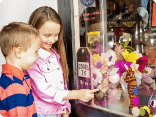 Two happy children point at the colorful, handcrafted items displayed in a shop window.