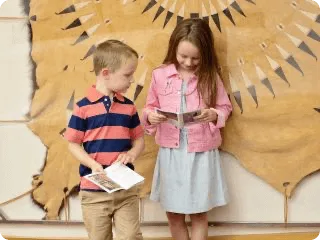 A young boy and girl read informational brochures in front of a traditional leather sunburst decoration.